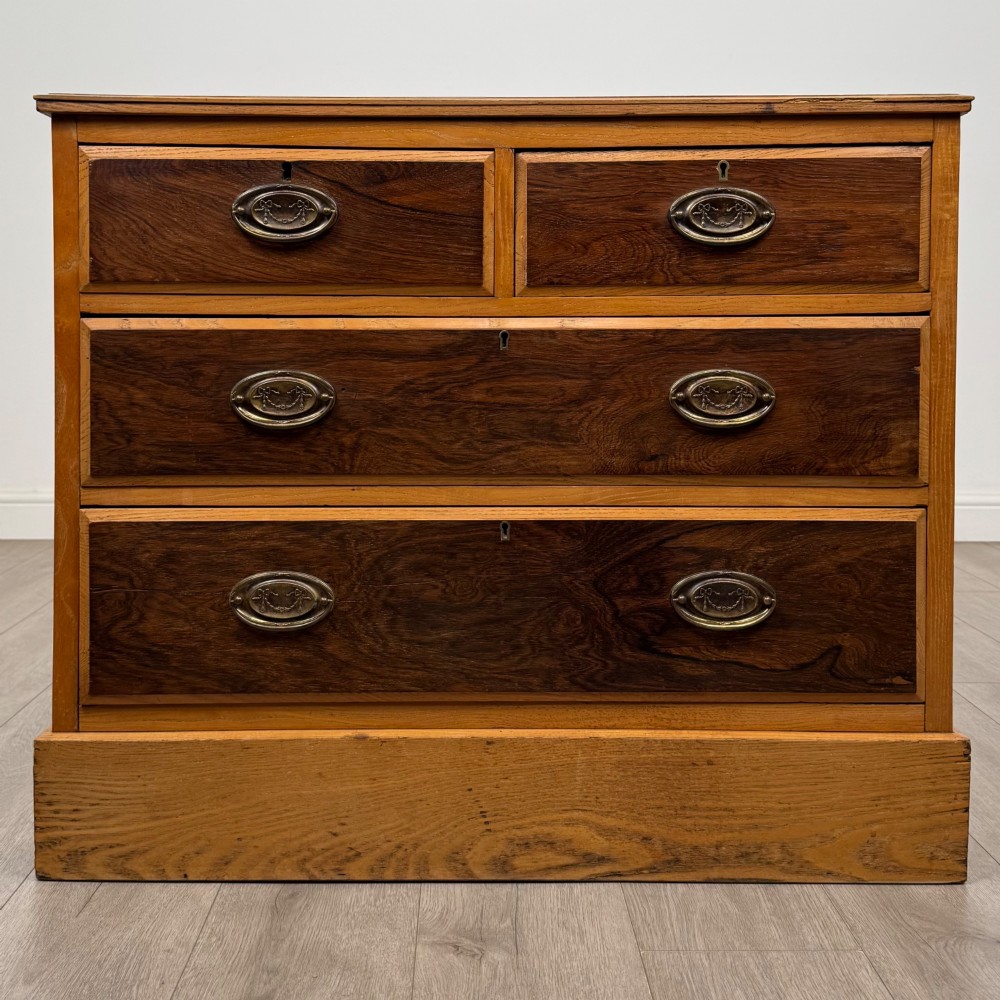 An antique Victorian oak chest of drawers featuring two short top drawers over two long lower drawers with dark drawer fronts, brass oval handles, and a plinth base.