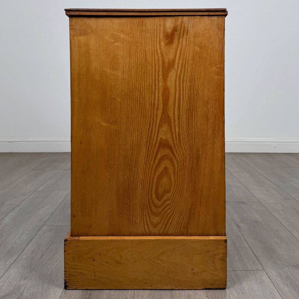 An antique Victorian oak chest of drawers featuring two short top drawers over two long lower drawers with dark drawer fronts, brass oval handles, and a plinth base. View III