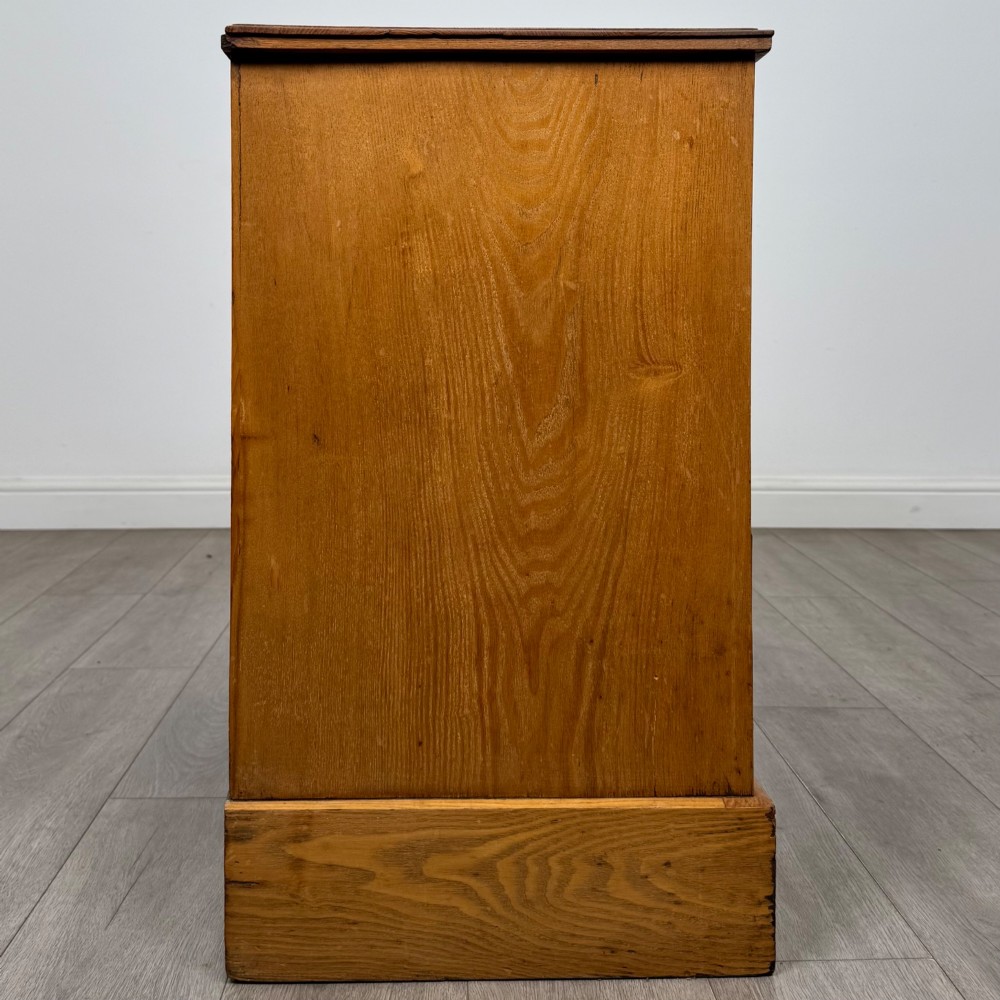 An antique Victorian oak chest of drawers featuring two short top drawers over two long lower drawers with dark drawer fronts, brass oval handles, and a plinth base. View VII