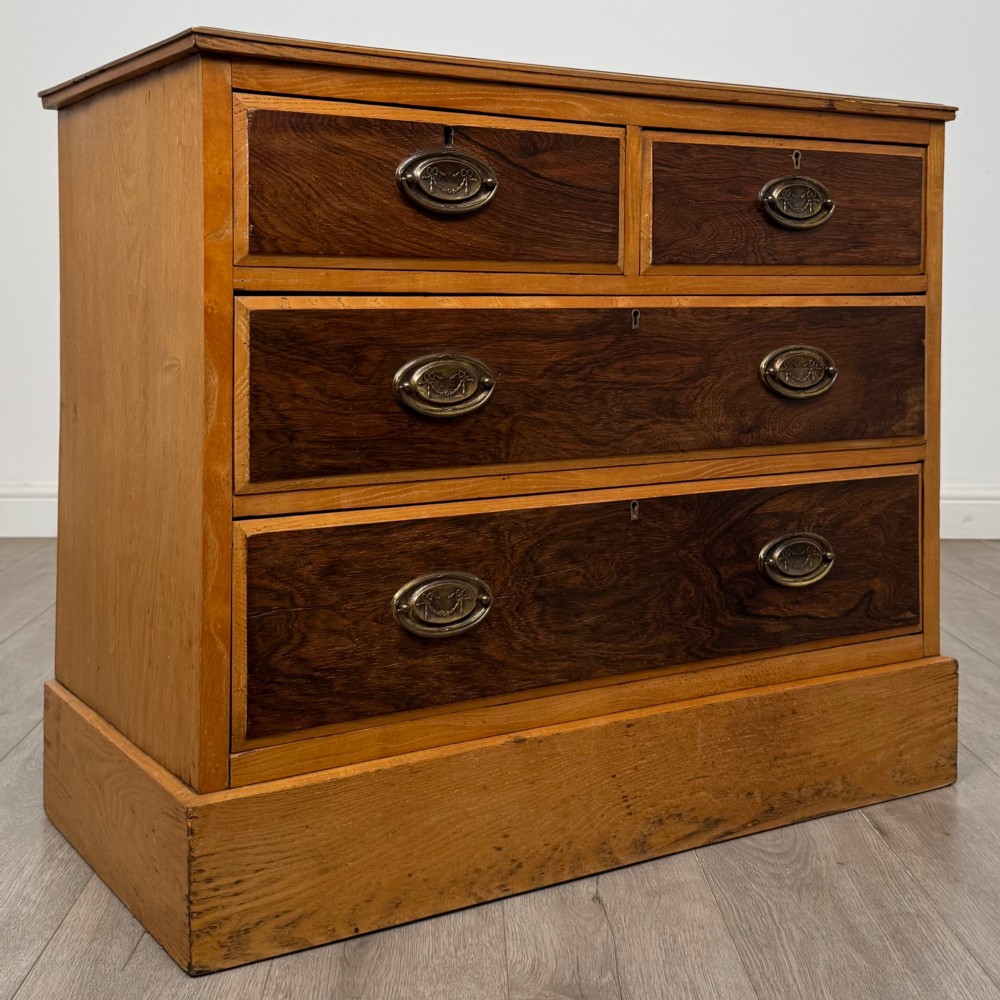 An antique Victorian oak chest of drawers featuring two short top drawers over two long lower drawers with dark drawer fronts, brass oval handles, and a plinth base. View VIII