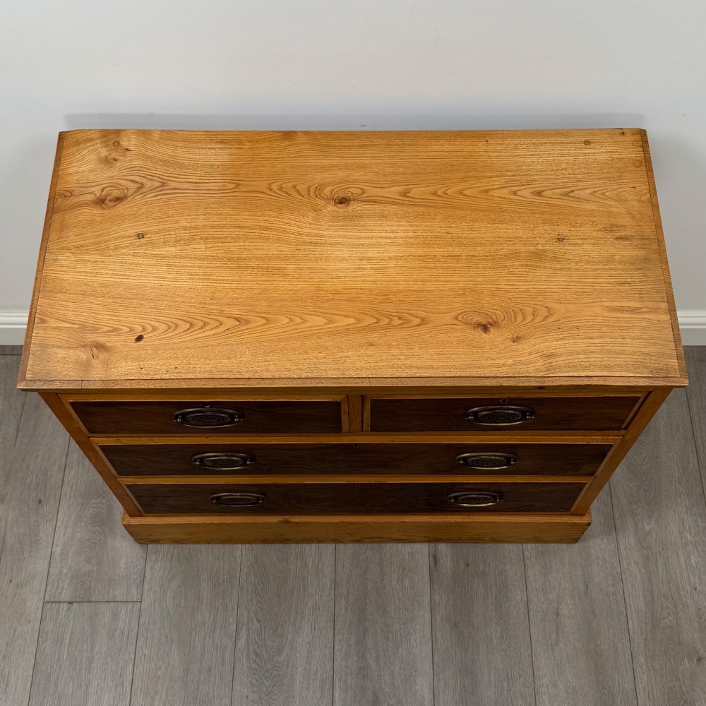An antique Victorian oak chest of drawers featuring two short top drawers over two long lower drawers with dark drawer fronts, brass oval handles, and a plinth base. View IX