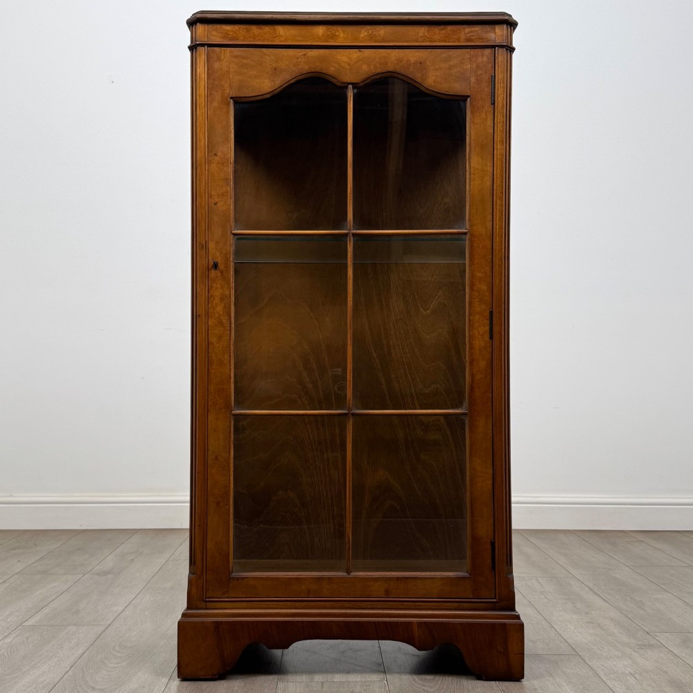 A freestanding burr walnut display cabinet featuring a single glazed door with six glass panes, curved upper frame moulding, and a bracket base.
