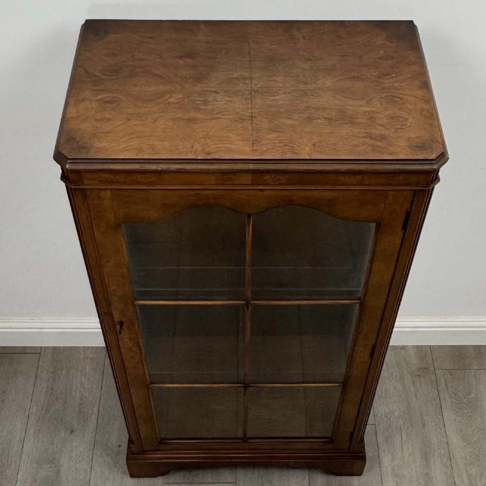 A freestanding burr walnut display cabinet featuring a single glazed door with six glass panes, curved upper frame moulding, and a bracket base. View X