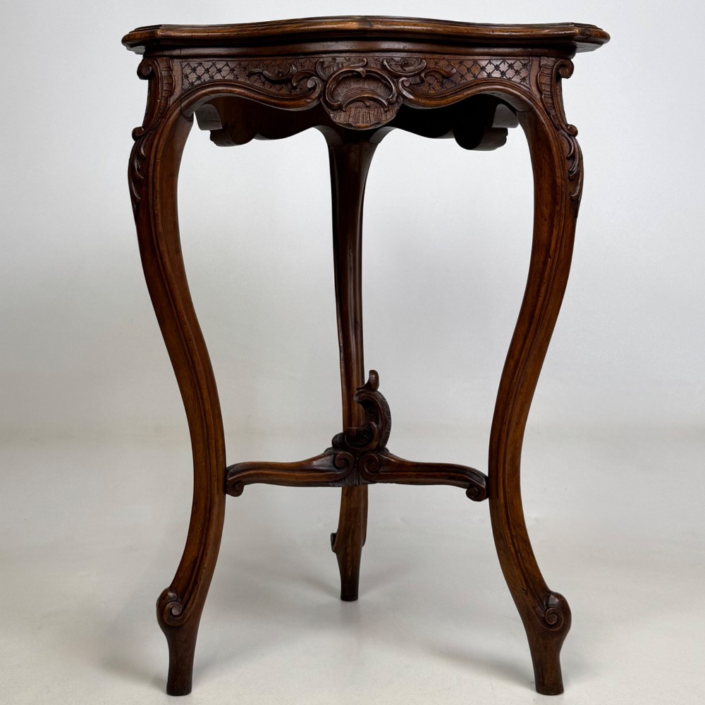 A dark mahogany side table featuring carved cabriole legs, a decorative carved apron with a shell motif, and a sculpted lower cross stretcher.