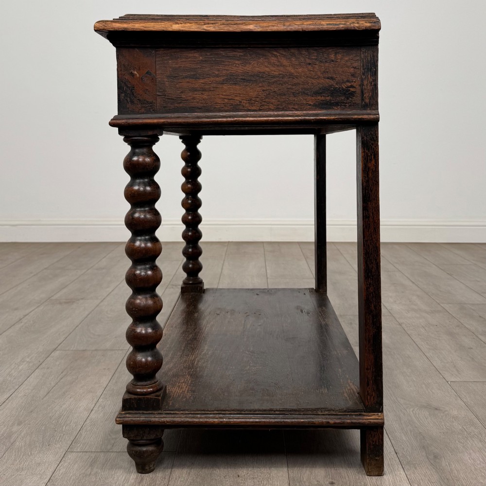 A dark oak Victorian side table featuring bobbin-turned legs, a lower shelf, and a carved frieze with a central mask motif. View III