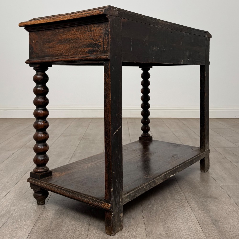 A dark oak Victorian side table featuring bobbin-turned legs, a lower shelf, and a carved frieze with a central mask motif. View IV