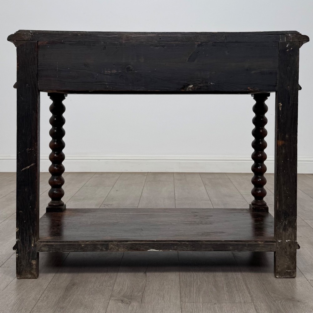 A dark oak Victorian side table featuring bobbin-turned legs, a lower shelf, and a carved frieze with a central mask motif. View V