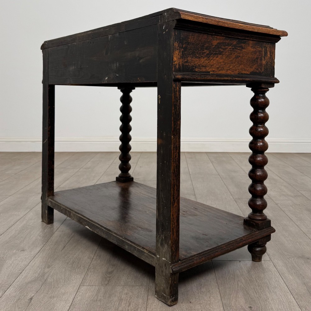 A dark oak Victorian side table featuring bobbin-turned legs, a lower shelf, and a carved frieze with a central mask motif. View VI