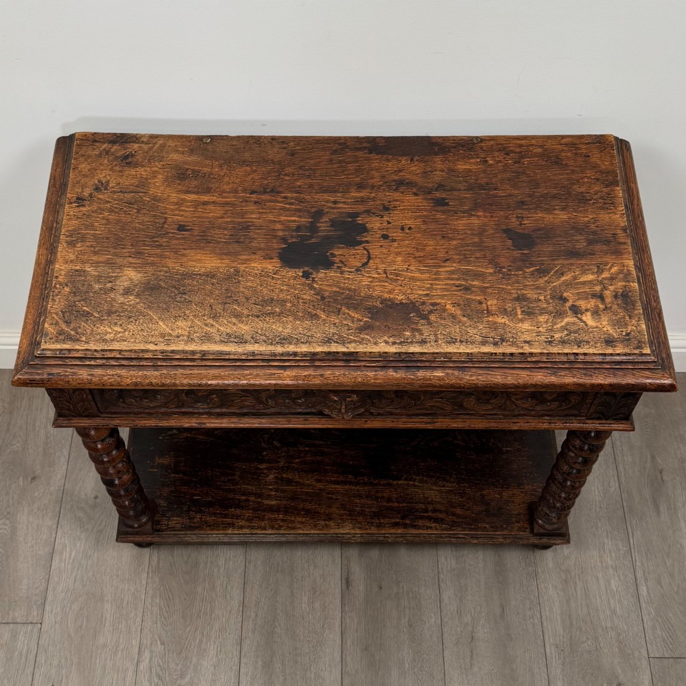 A dark oak Victorian side table featuring bobbin-turned legs, a lower shelf, and a carved frieze with a central mask motif. View IX