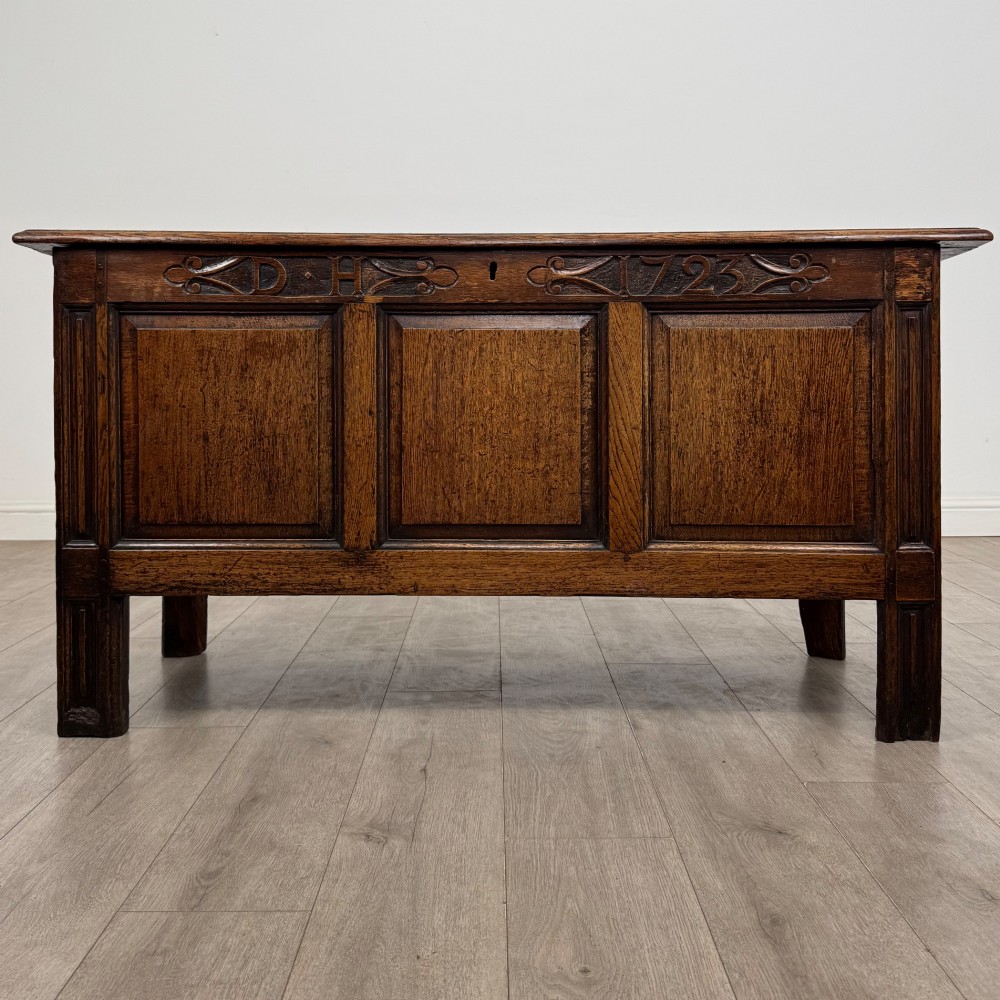 An 18th-century Georgian golden oak coffer featuring three raised panel front section and a carved top rail dated 1723 with initials D H.
