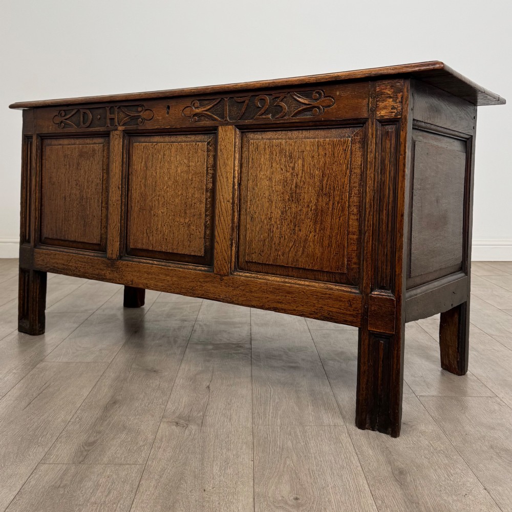 An 18th-century Georgian golden oak coffer featuring three raised panel front section and a carved top rail dated 1723 with initials D H. View II