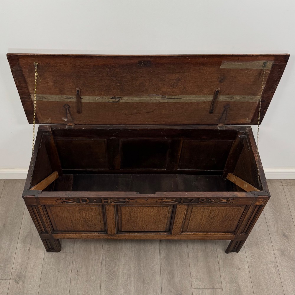 An 18th-century Georgian golden oak coffer featuring three raised panel front section and a carved top rail dated 1723 with initials D H. View X