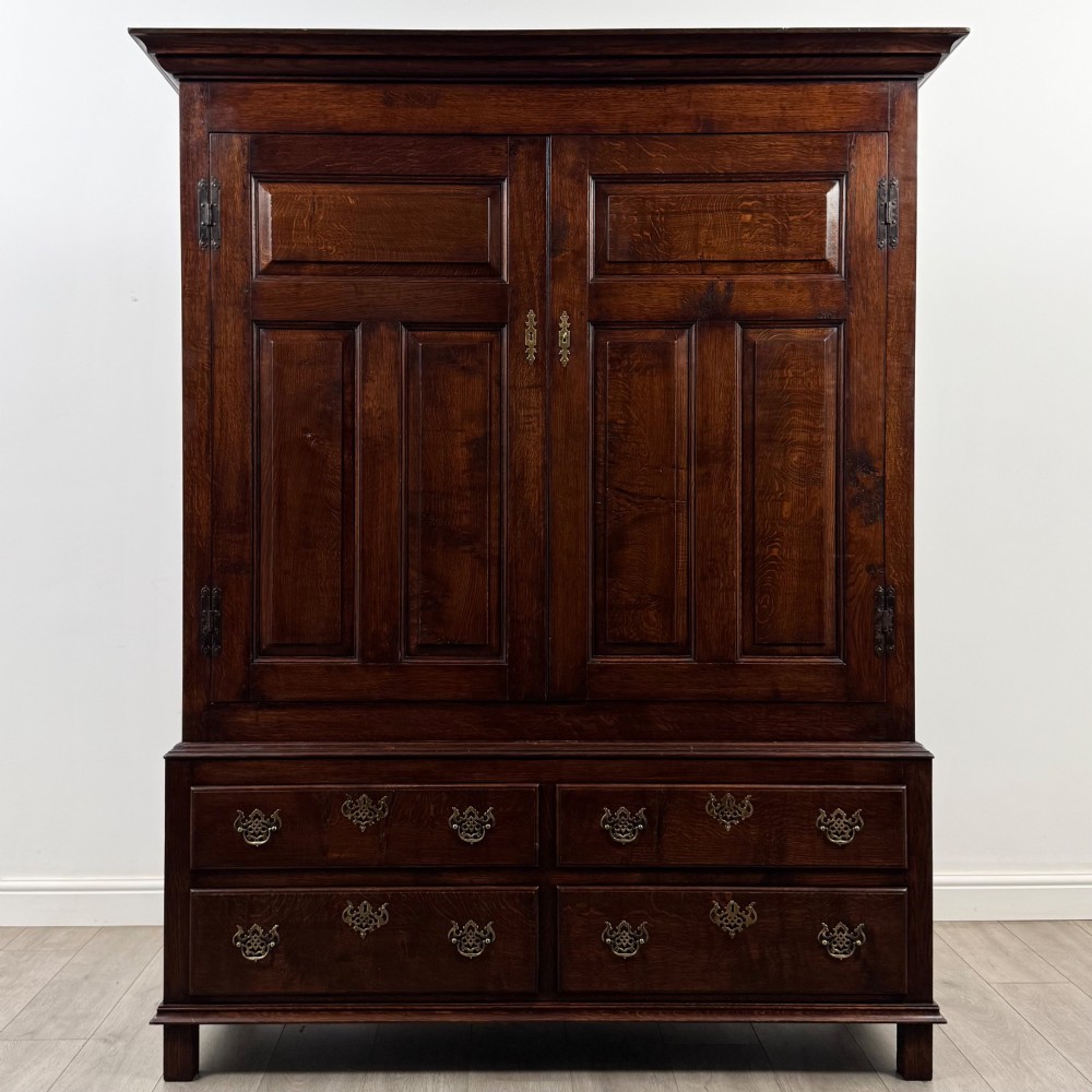 A dark oak double wardrobe featuring panelled doors set above four drawers with decorative brass drop handles.