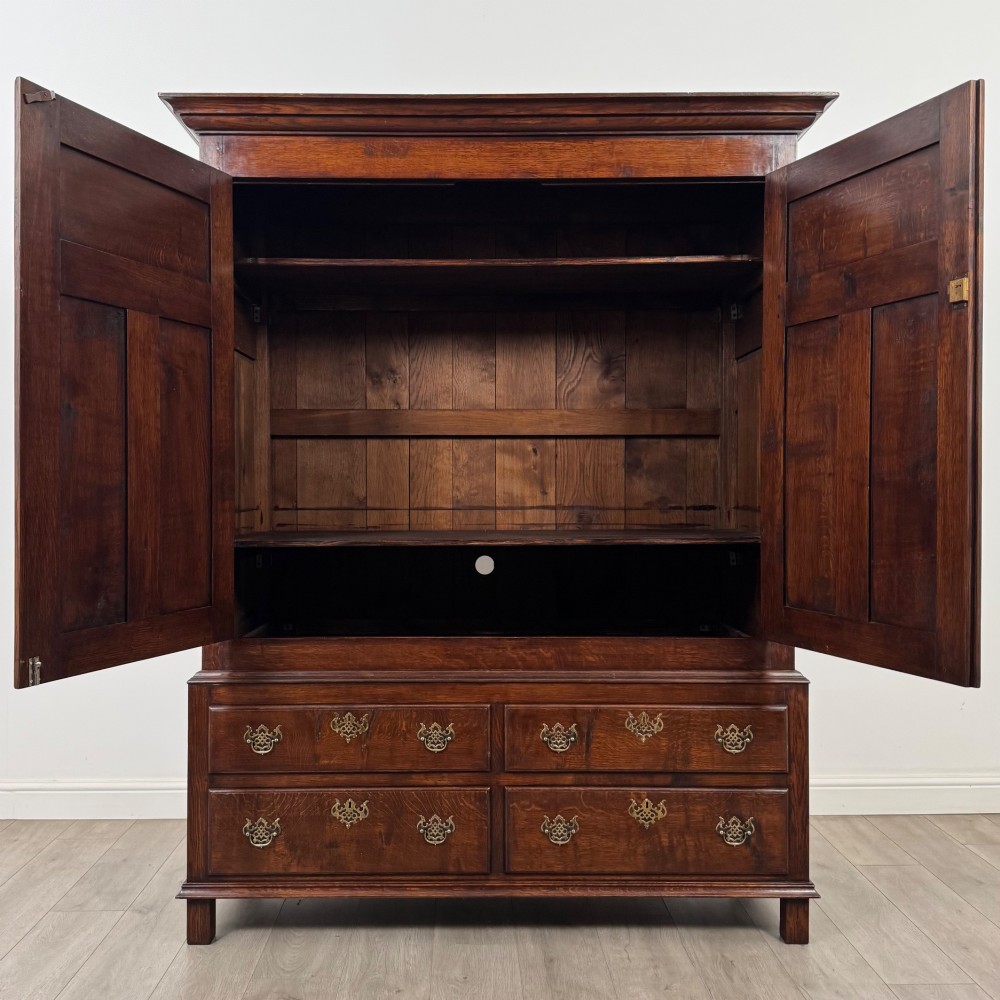 A dark oak double wardrobe featuring panelled doors set above four drawers with decorative brass drop handles. View II