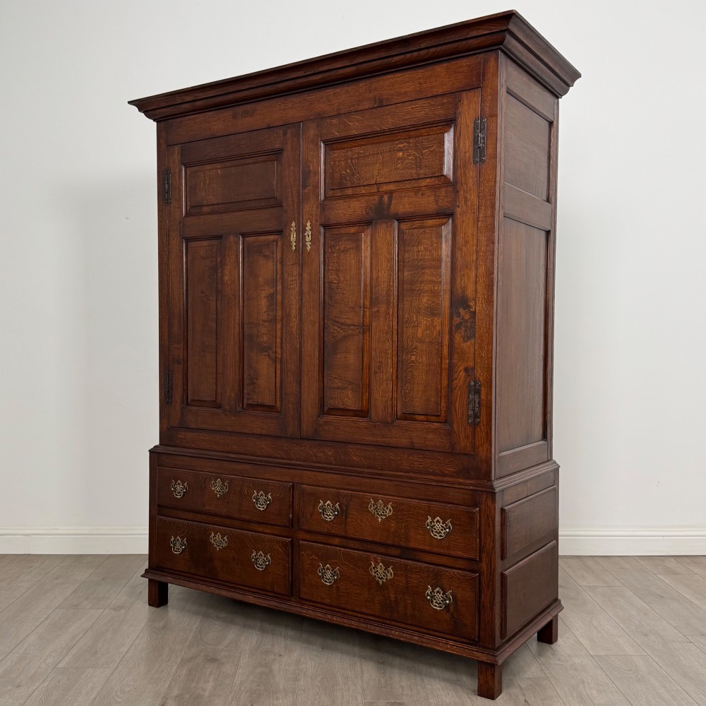 A dark oak double wardrobe featuring panelled doors set above four drawers with decorative brass drop handles. View III