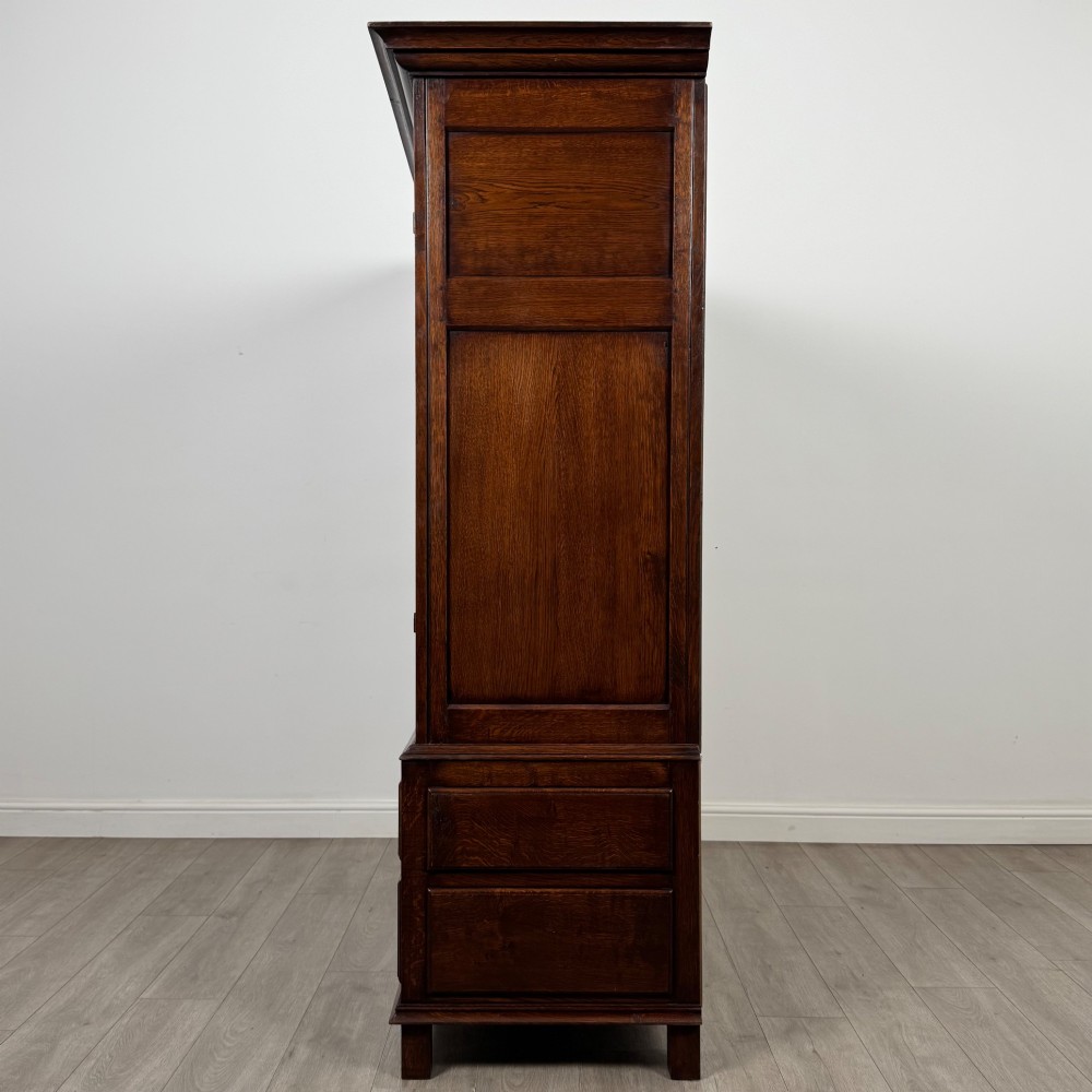 A dark oak double wardrobe featuring panelled doors set above four drawers with decorative brass drop handles. View IV