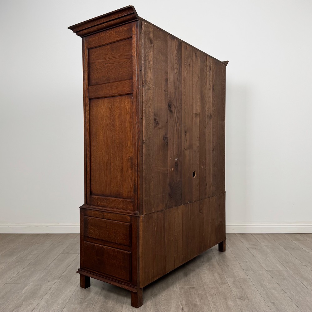A dark oak double wardrobe featuring panelled doors set above four drawers with decorative brass drop handles. View V