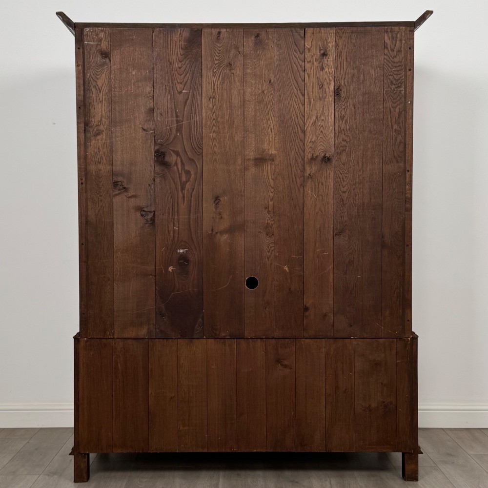 A dark oak double wardrobe featuring panelled doors set above four drawers with decorative brass drop handles. View VI