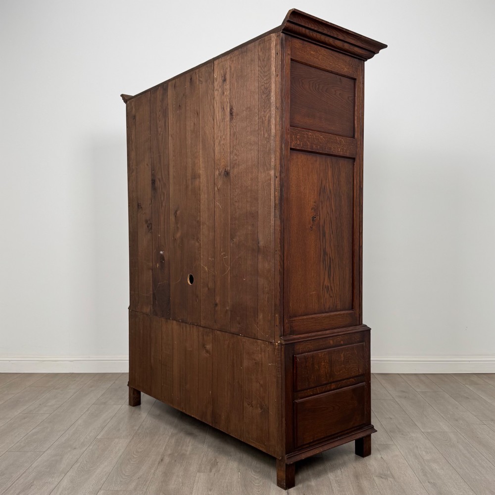 A dark oak double wardrobe featuring panelled doors set above four drawers with decorative brass drop handles. View VII