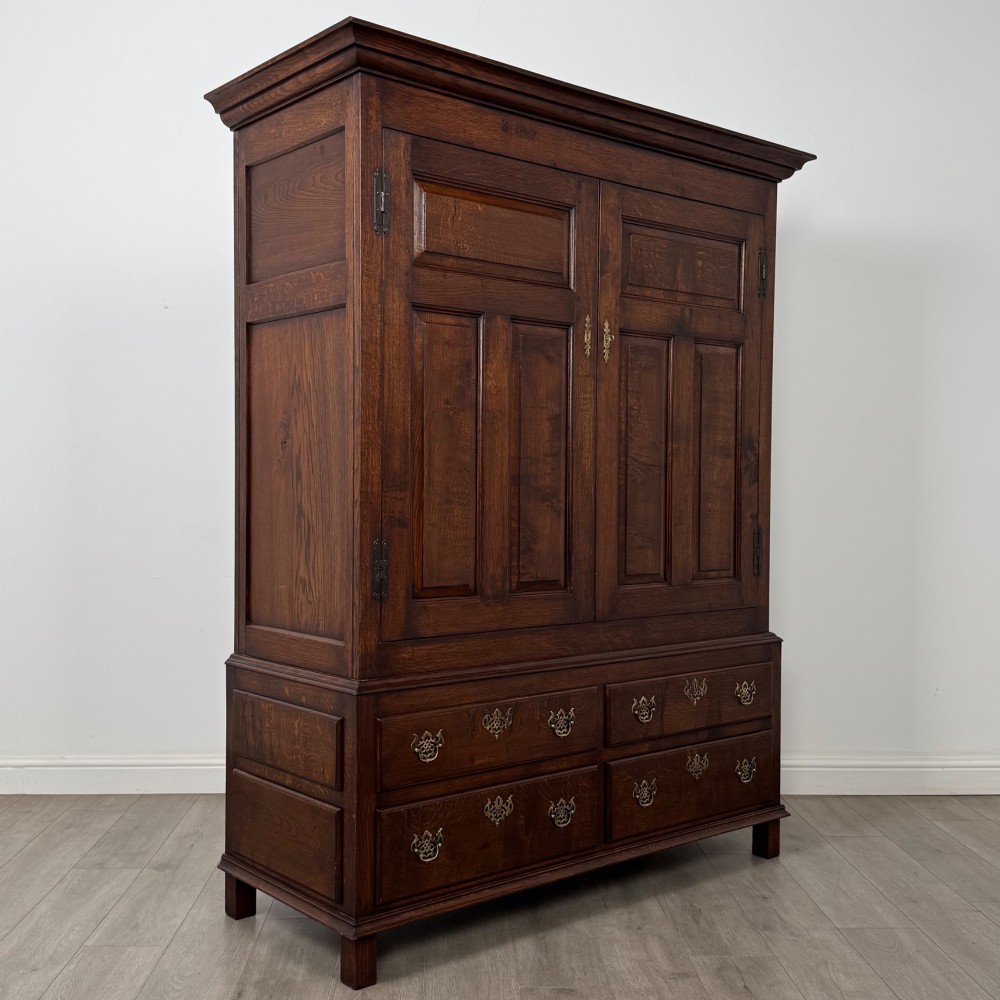 A dark oak double wardrobe featuring panelled doors set above four drawers with decorative brass drop handles. View IX