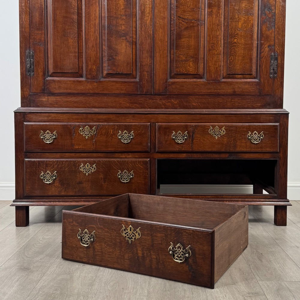 A dark oak double wardrobe featuring panelled doors set above four drawers with decorative brass drop handles. View X
