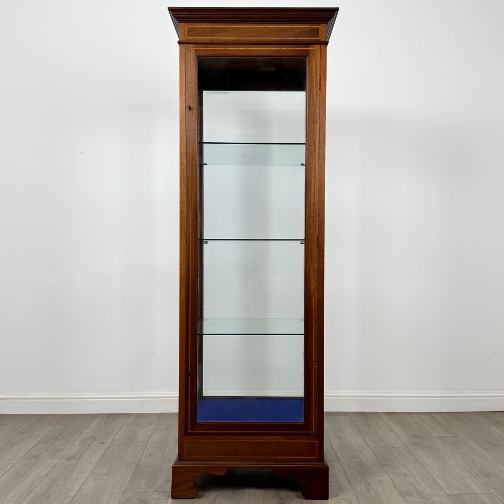 A tall early twentieth-century mahogany display cabinet featuring glazed sides, glass shelves, geometric string inlay, and bracket feet.