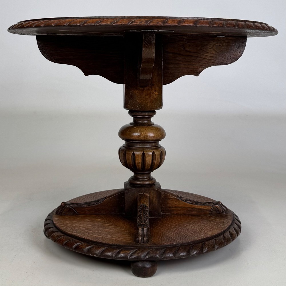 A round dark oak coffee table featuring a carved edge, a turned central pedestal, and a circular base supported on bun feet. View II