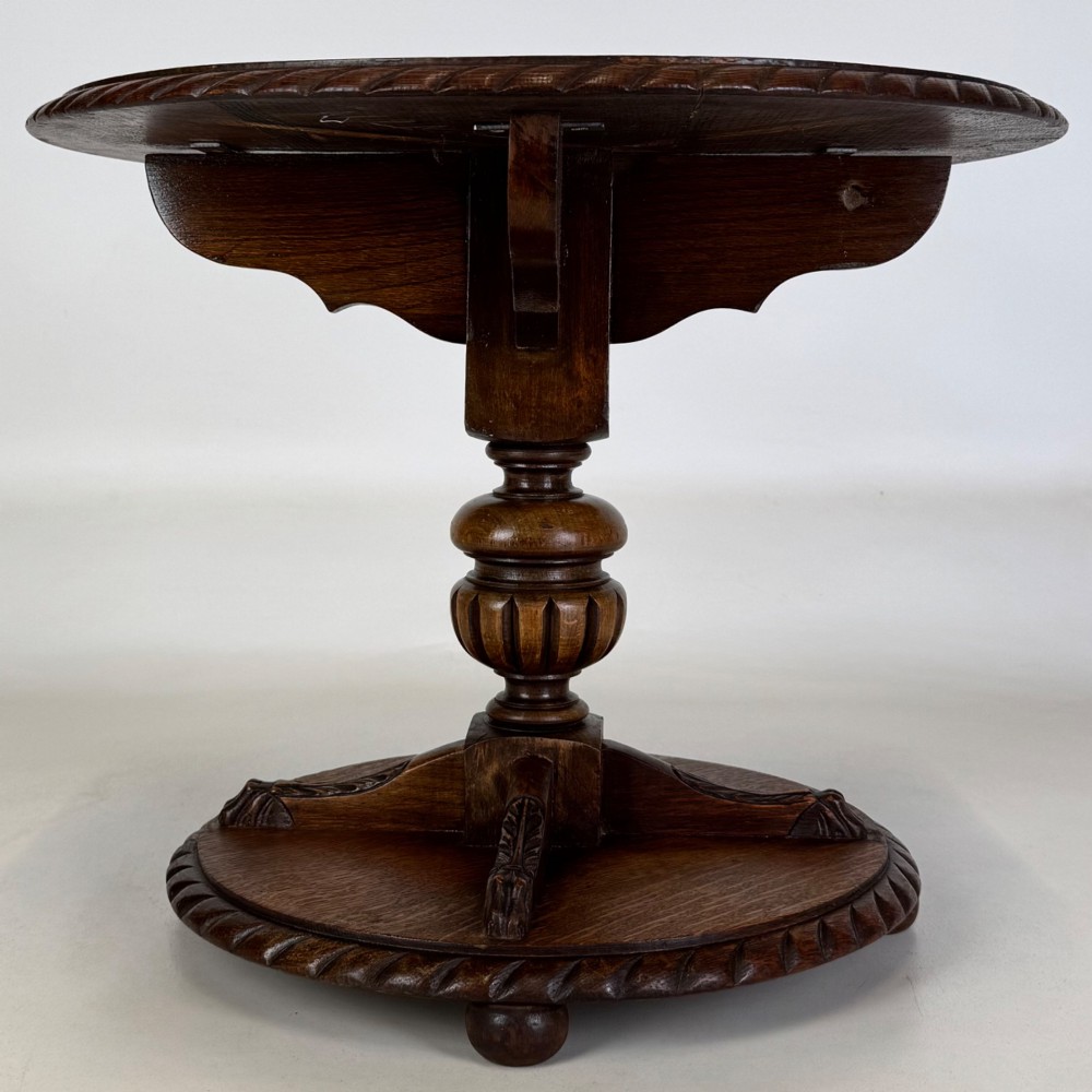 A round dark oak coffee table featuring a carved edge, a turned central pedestal, and a circular base supported on bun feet. View IV