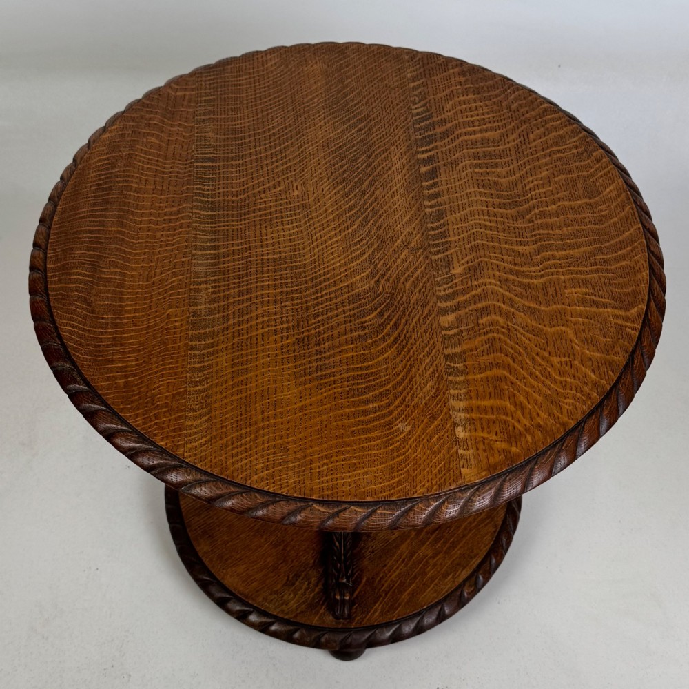 A round dark oak coffee table featuring a carved edge, a turned central pedestal, and a circular base supported on bun feet. View V