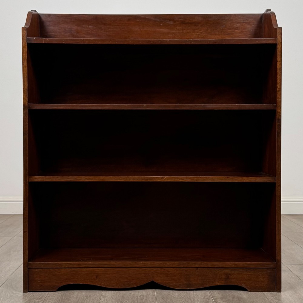 A dark mahogany open bookcase featuring three broad fixed shelves, shaped gallery side panels, and a subtle wave-formed lower apron. View II