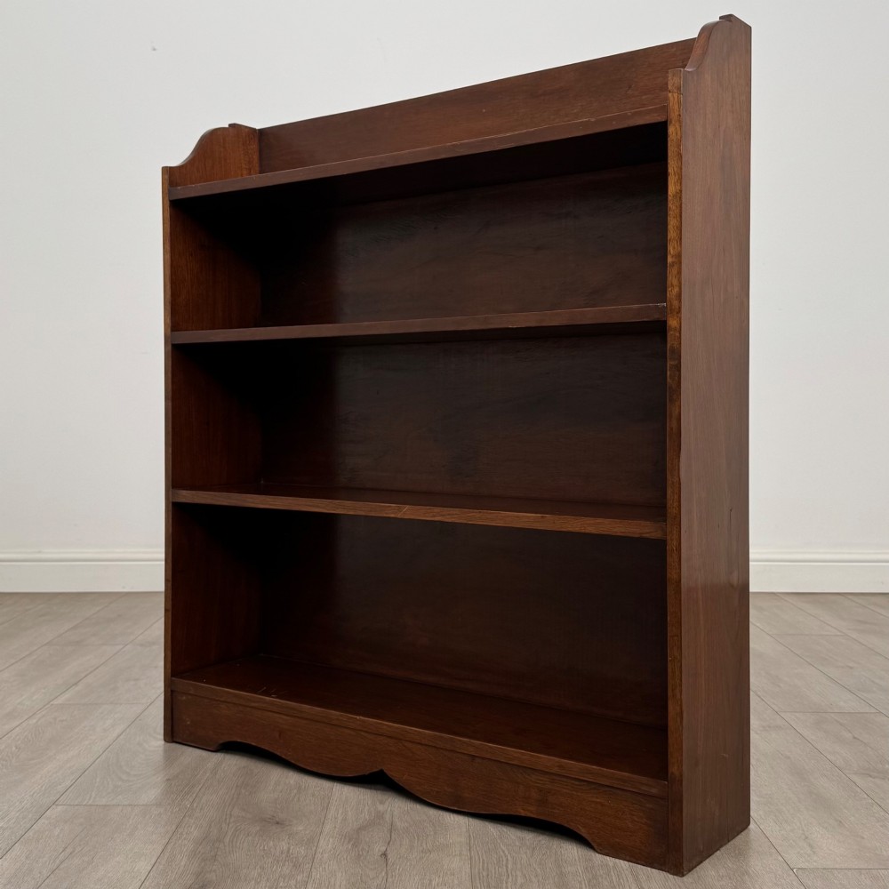 A dark mahogany open bookcase featuring three broad fixed shelves, shaped gallery side panels, and a subtle wave-formed lower apron. View III