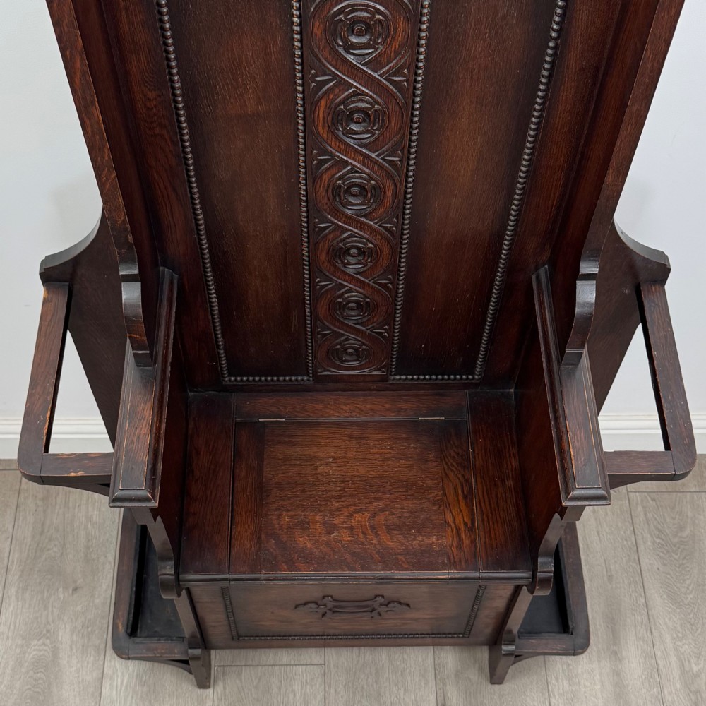A tall dark oak Edwardian hall stand featuring carved panels, turned coat pegs, a central mirror, a lift-top storage seat, and umbrella holders on both sides. View IX