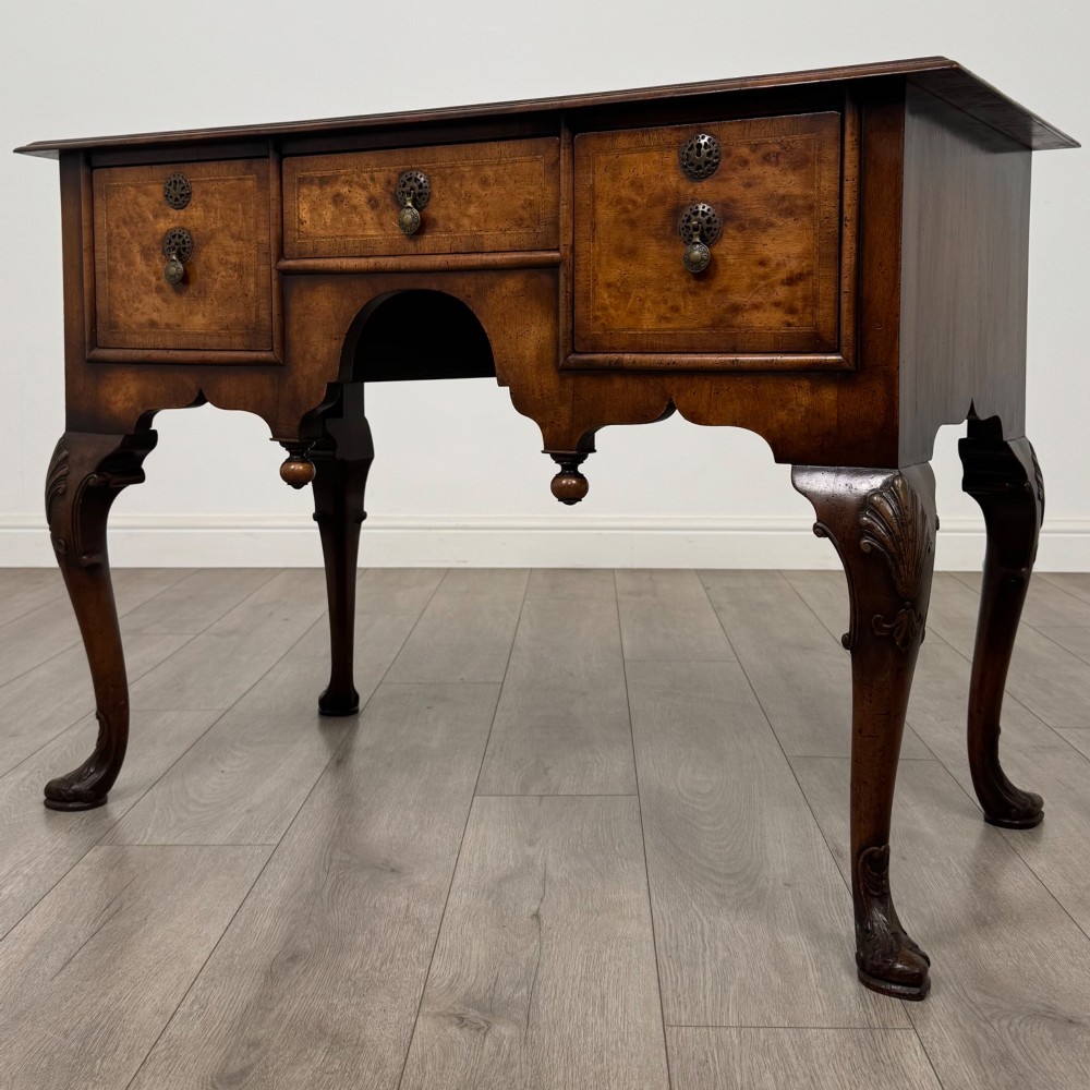 A Queen Anne style burr walnut writing table featuring cabriole legs, three front drawers with brass drop handles, and an arched kneehole. View II