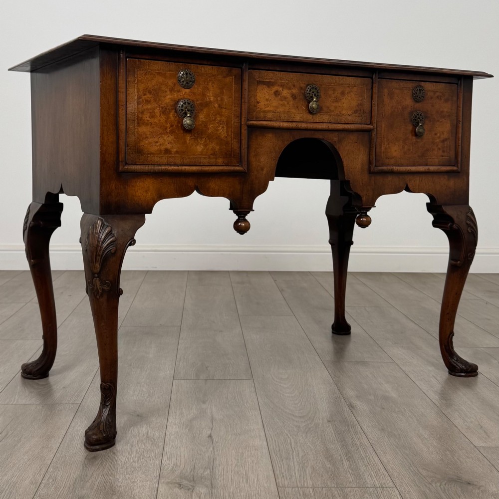 A Queen Anne style burr walnut writing table featuring cabriole legs, three front drawers with brass drop handles, and an arched kneehole. View VIII