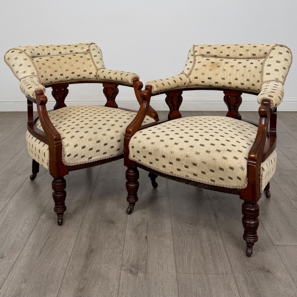 A pair of Edwardian mahogany tub chairs upholstered in a patterned cream fabric with turned front legs on castors.