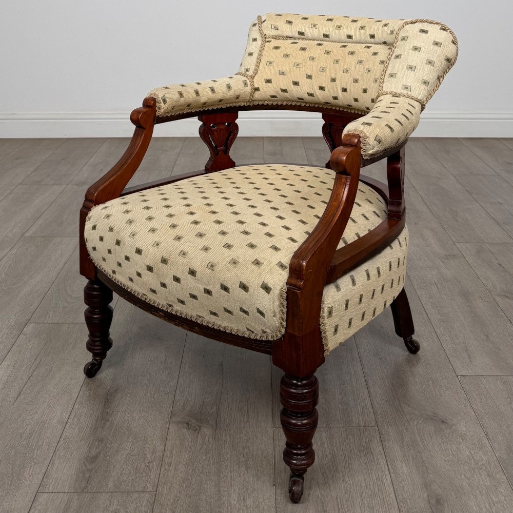A pair of Edwardian mahogany tub chairs upholstered in a patterned cream fabric with turned front legs on castors. View II