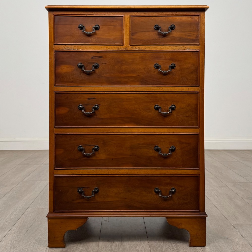 A tall 20th-century yew wood chest of drawers featuring two short drawers over four long graduated drawers with brass drop handles and bracket feet.