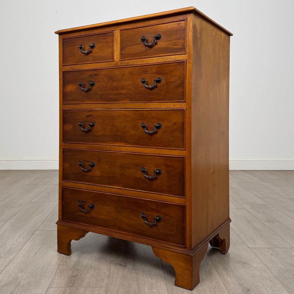 A tall 20th-century yew wood chest of drawers featuring two short drawers over four long graduated drawers with brass drop handles and bracket feet. View II