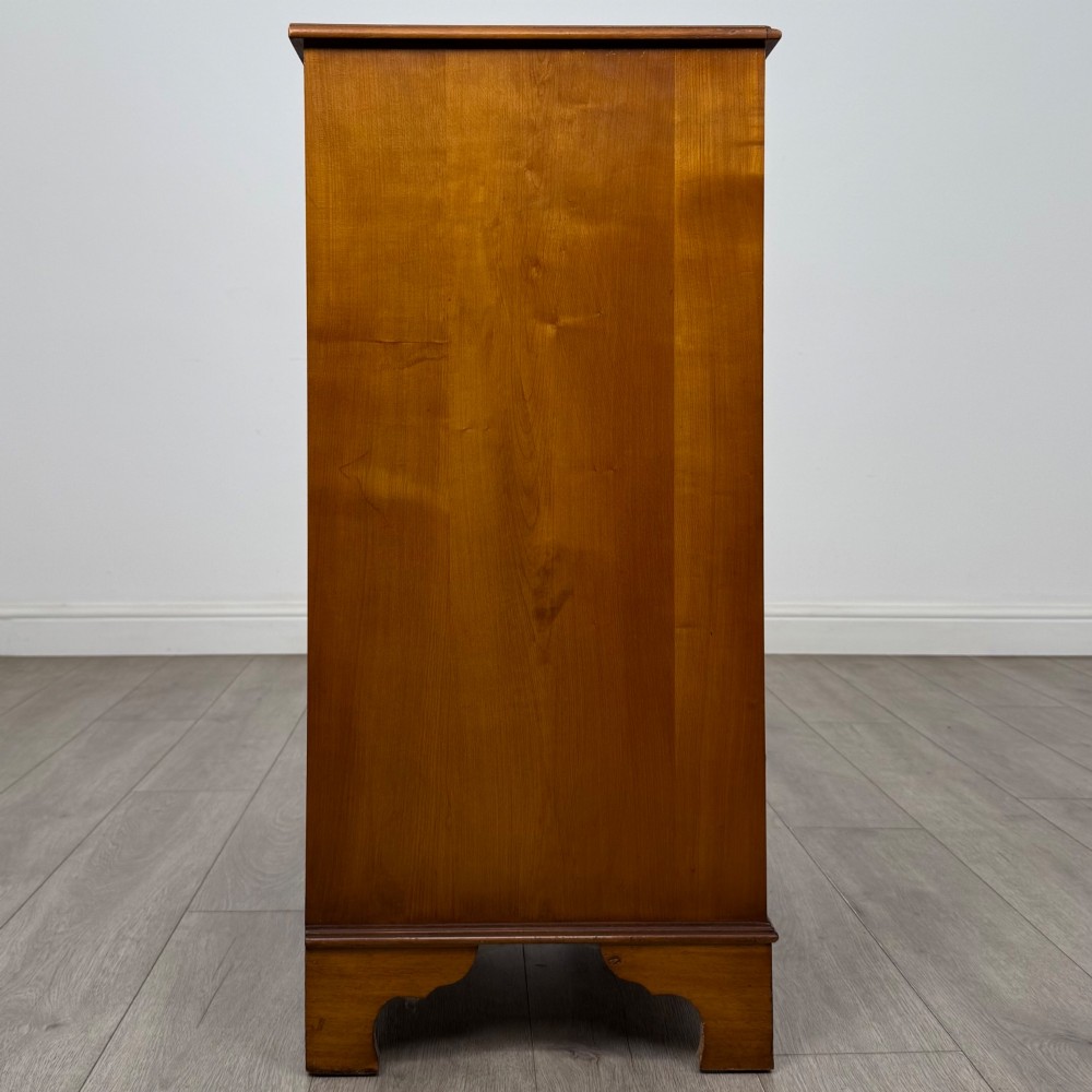 A tall 20th-century yew wood chest of drawers featuring two short drawers over four long graduated drawers with brass drop handles and bracket feet. View VII