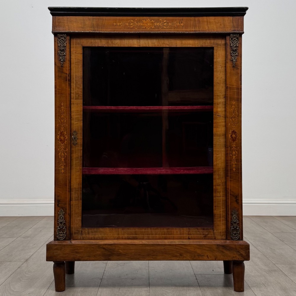 A 19th-century Victorian walnut pier cabinet featuring floral marquetry inlay, gilt brass mounts, and a single glazed door revealing lined interior shelves.