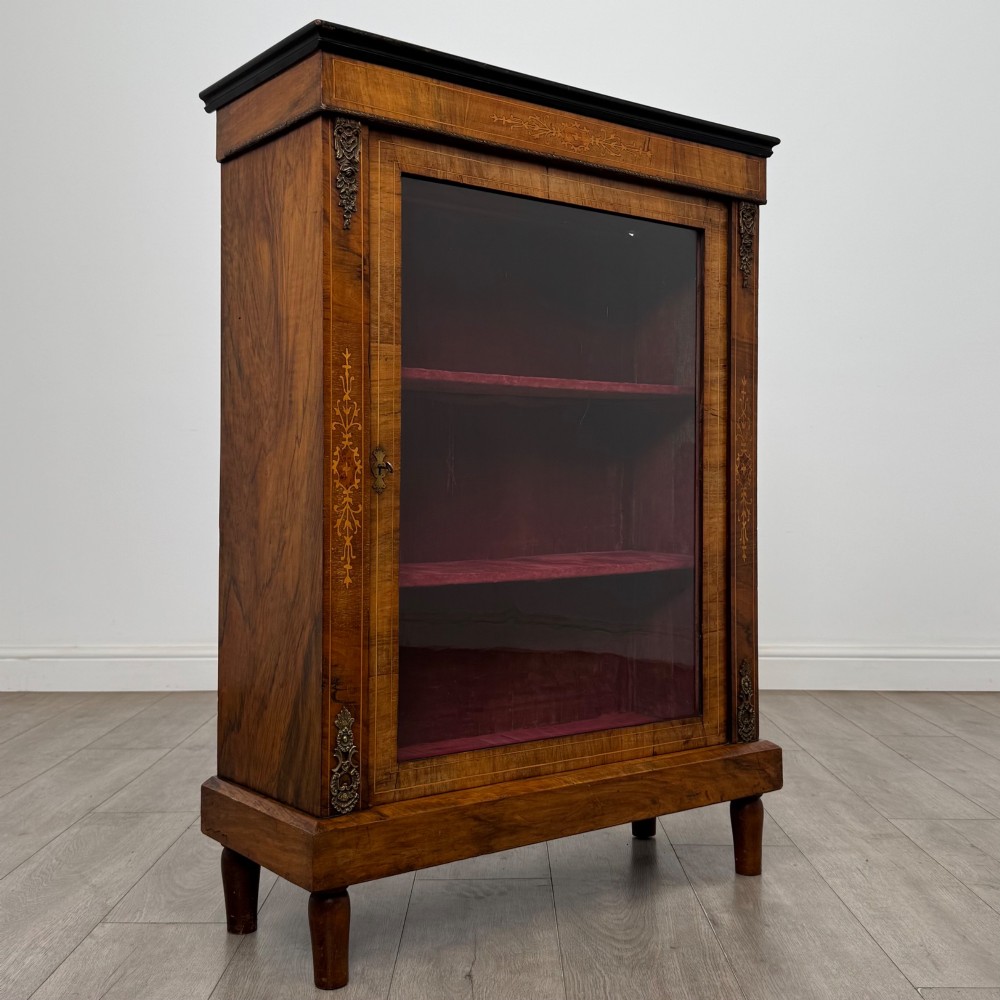 A 19th-century Victorian walnut pier cabinet featuring floral marquetry inlay, gilt brass mounts, and a single glazed door revealing lined interior shelves. View IX