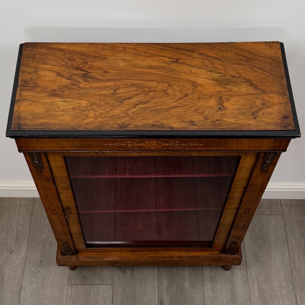 A 19th-century Victorian walnut pier cabinet featuring floral marquetry inlay, gilt brass mounts, and a single glazed door revealing lined interior shelves. View X