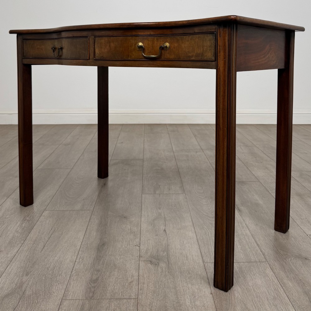 A 19th-century mahogany writing table with a curved serpentine front edge, two drawers with brass handles, and square legs. View II