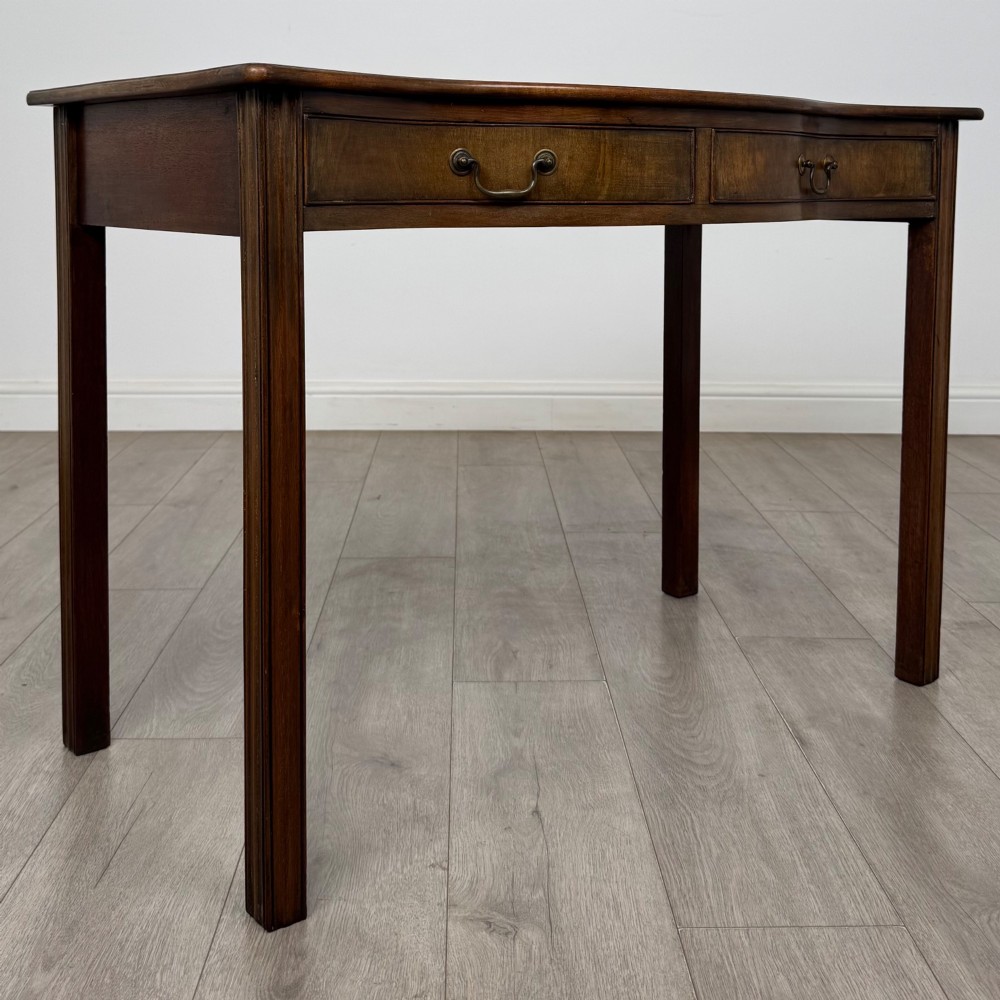 A 19th-century mahogany writing table with a curved serpentine front edge, two drawers with brass handles, and square legs. View VIII