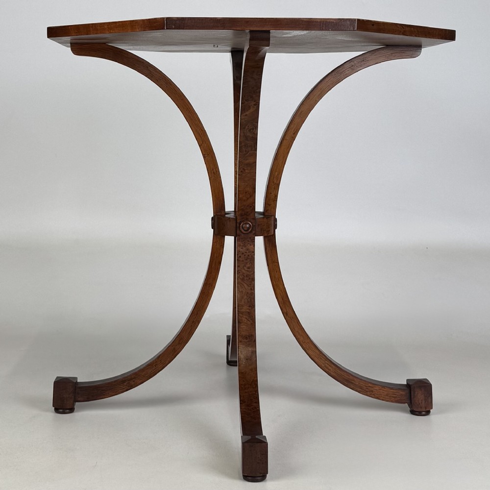 An octagonal side table crafted from burr walnut featuring four outward-curving legs joined by a central collar. View II