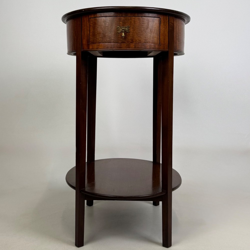 A tall Edwardian mahogany oval side table featuring a single top drawer with a brass handle and an oval lower undertier shelf.