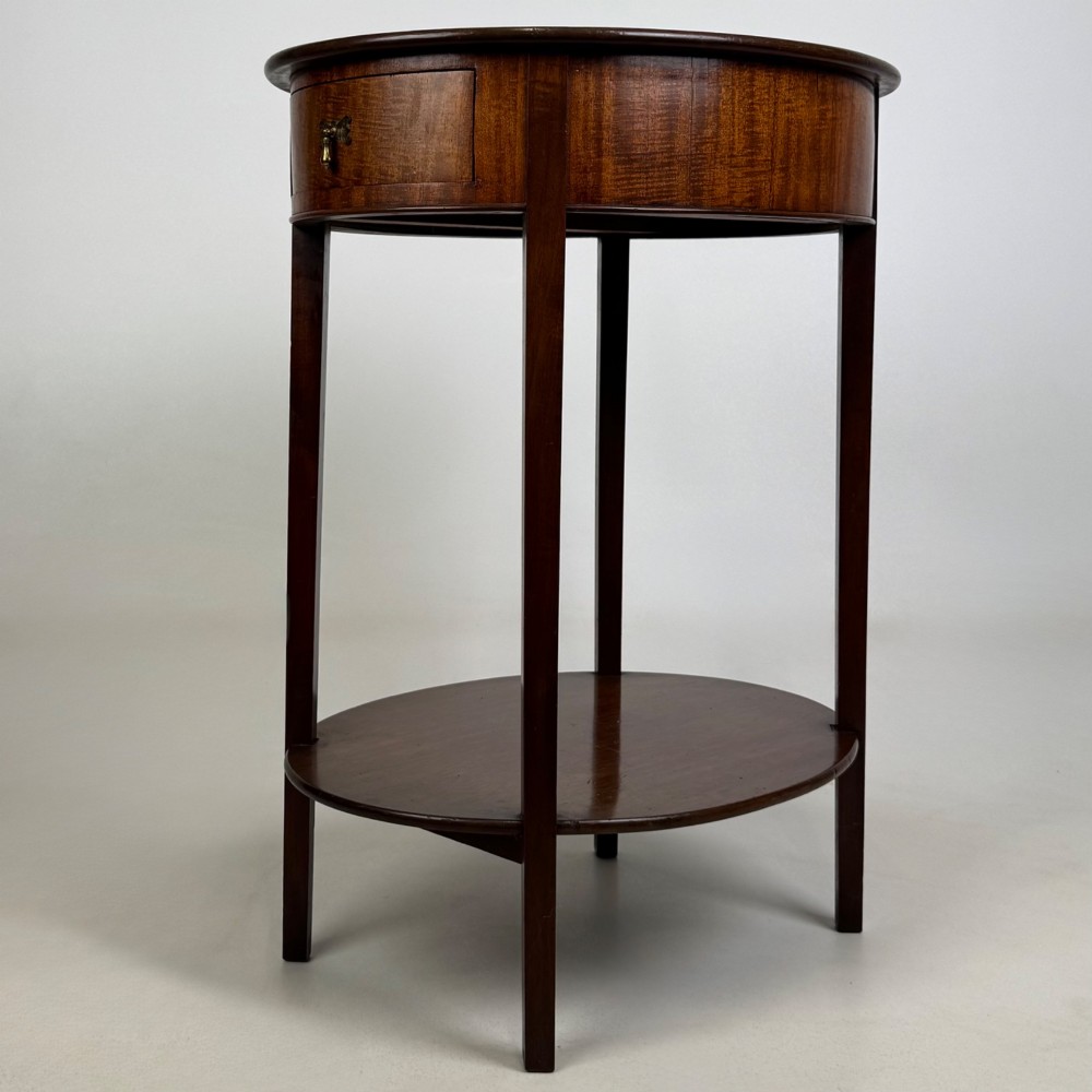 A tall Edwardian mahogany oval side table featuring a single top drawer with a brass handle and an oval lower undertier shelf. View II