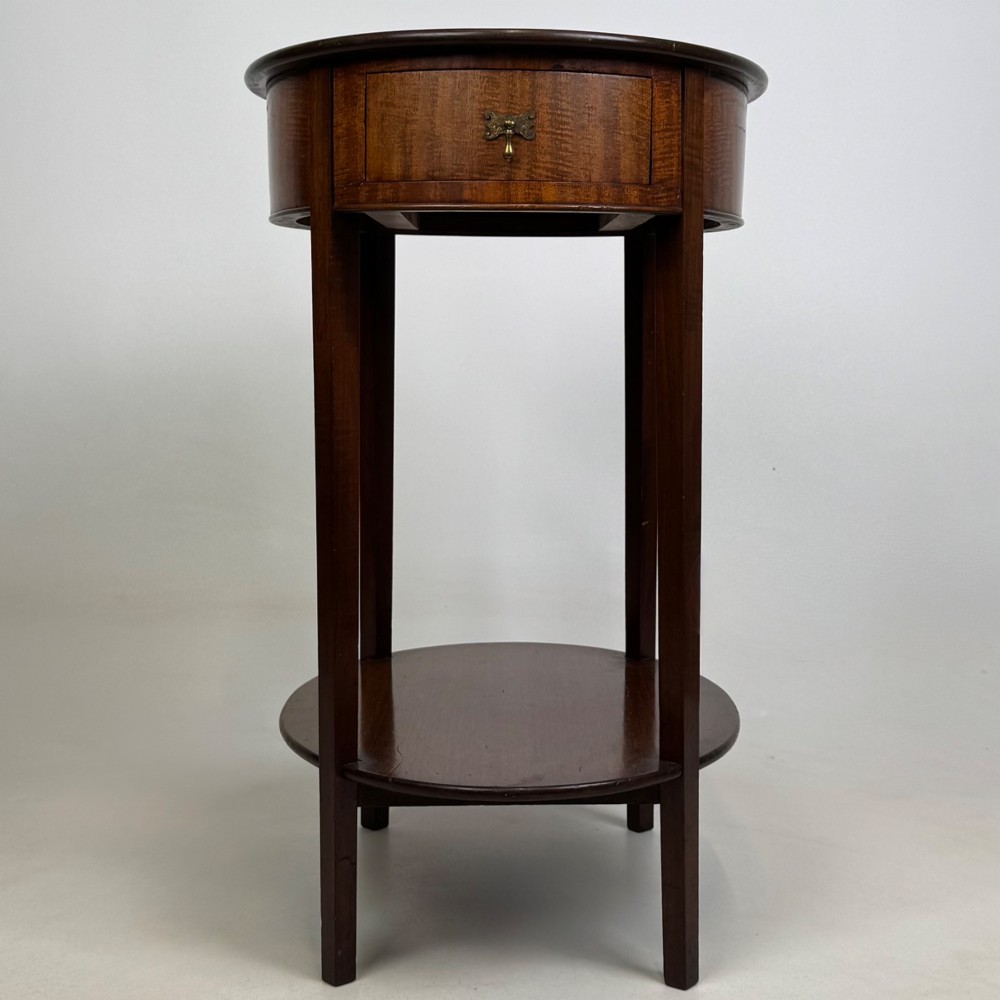 A tall Edwardian mahogany oval side table featuring a single top drawer with a brass handle and an oval lower undertier shelf. View V