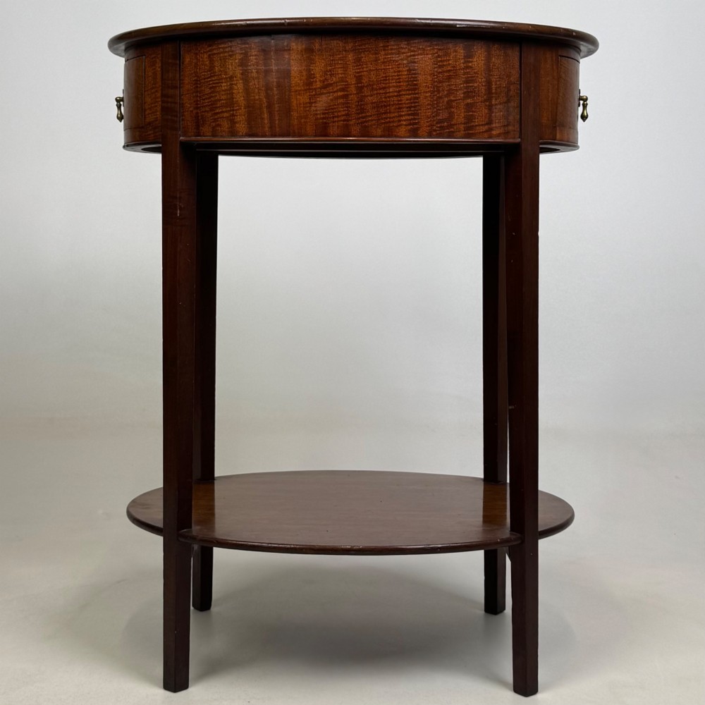 A tall Edwardian mahogany oval side table featuring a single top drawer with a brass handle and an oval lower undertier shelf. View VII