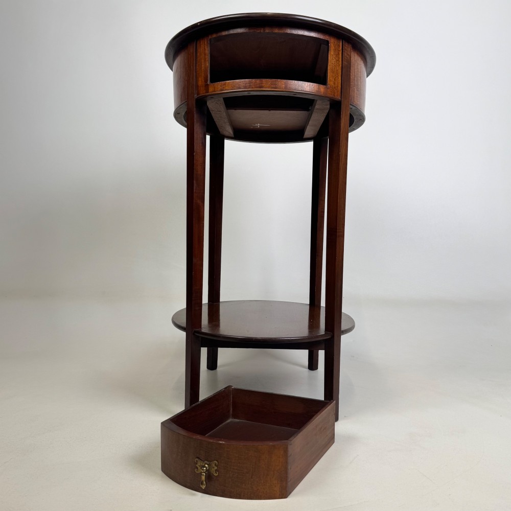 A tall Edwardian mahogany oval side table featuring a single top drawer with a brass handle and an oval lower undertier shelf. View X